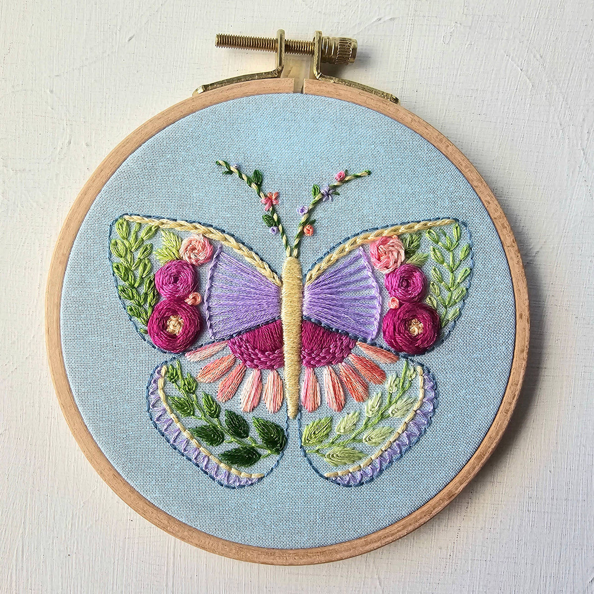 Close-up of the finished butterfly sampler embroidery in a wooden hoop