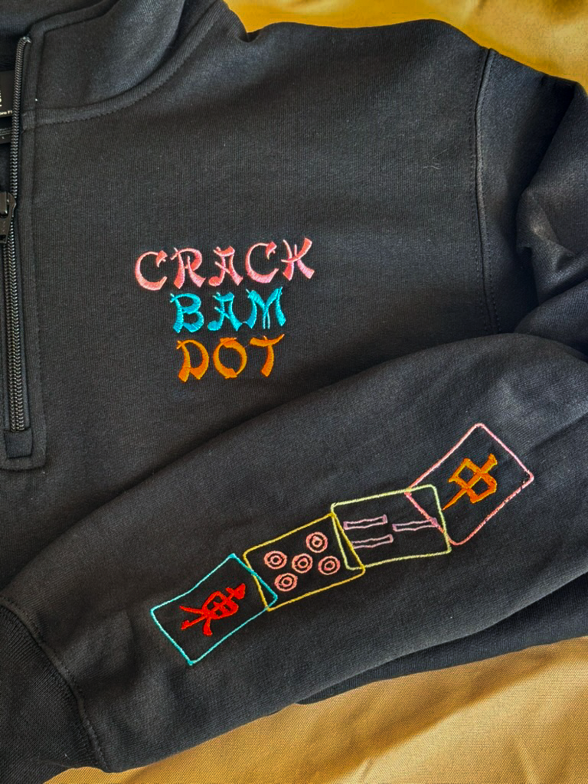 Black quarter zip embroidered CRACK BAM DOT with colorful mahjong tiles stitched down the sleeve