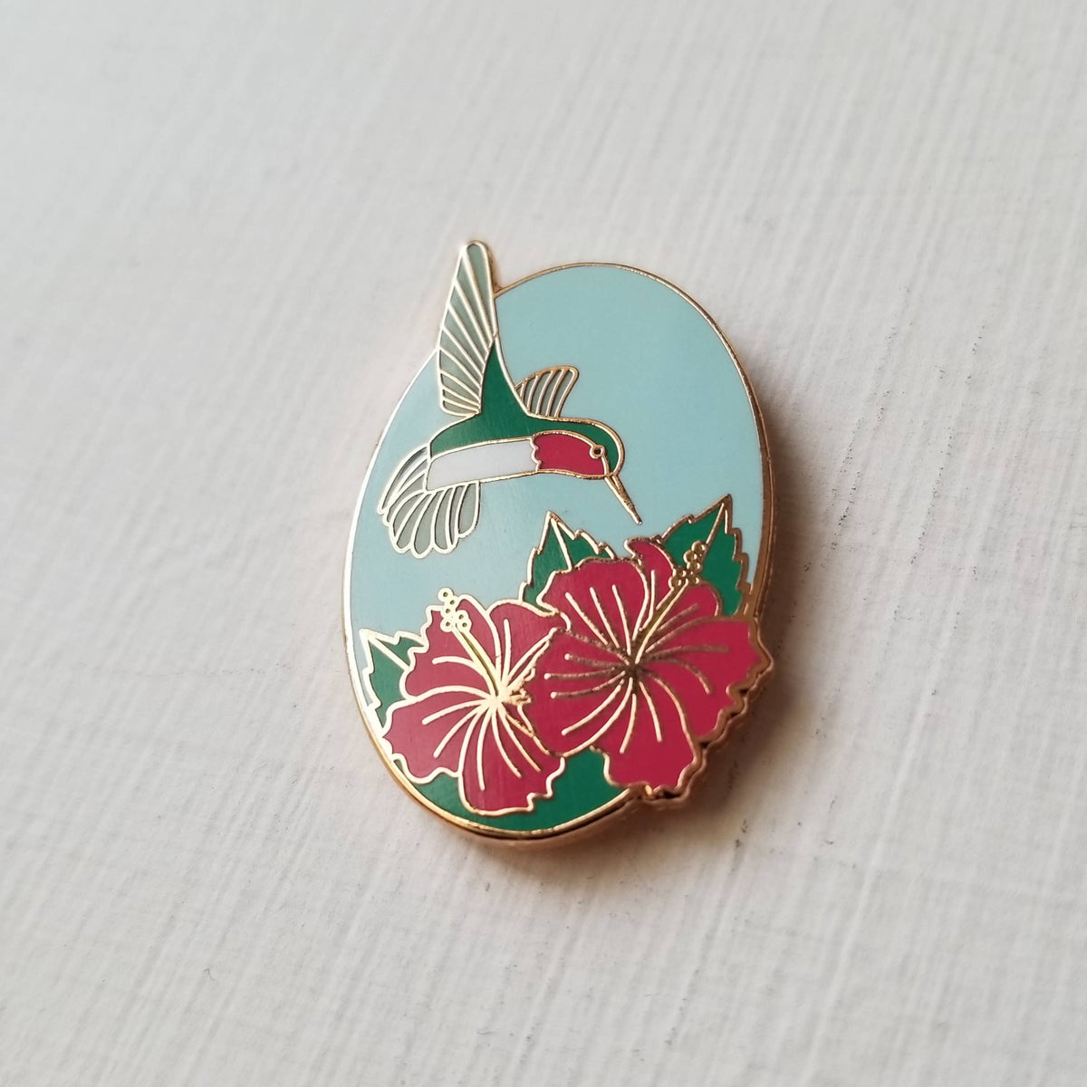 Angled view of the hummingbird and pink hibiscus enamel needle minder