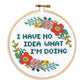 Finished cross stitch reading "I have no idea what I'm doing" in teal with coral and purple flowers in a wooden hoop