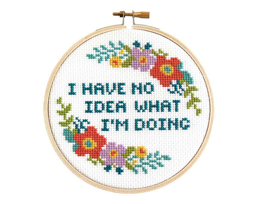 Finished cross stitch reading "I have no idea what I'm doing" in teal with coral and purple flowers in a wooden hoop