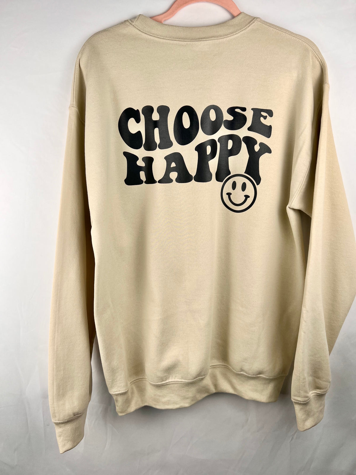Sand Choose Happy crewneck on a hanger showing the back print