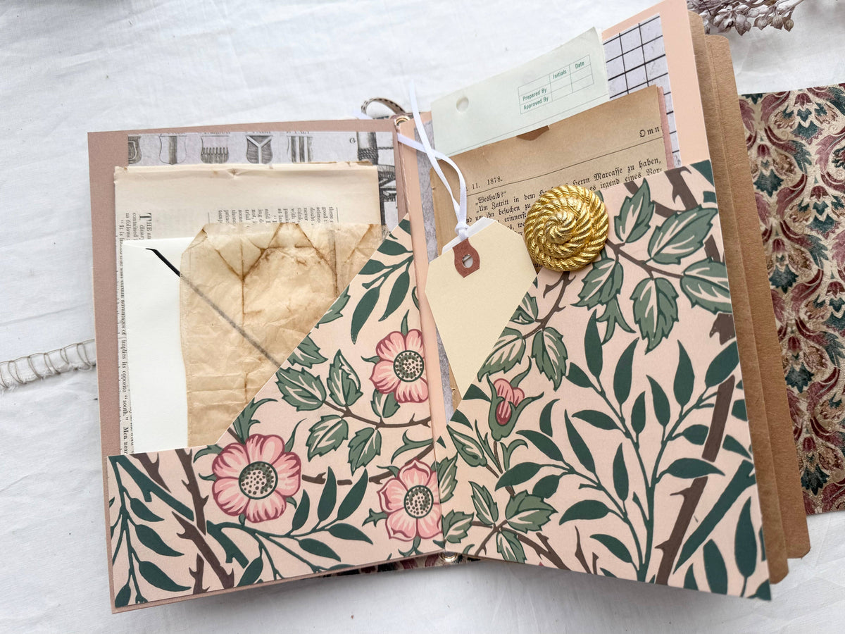 Open journal folio with a pink floral pocket, vintage book pages, a tag and a gold button