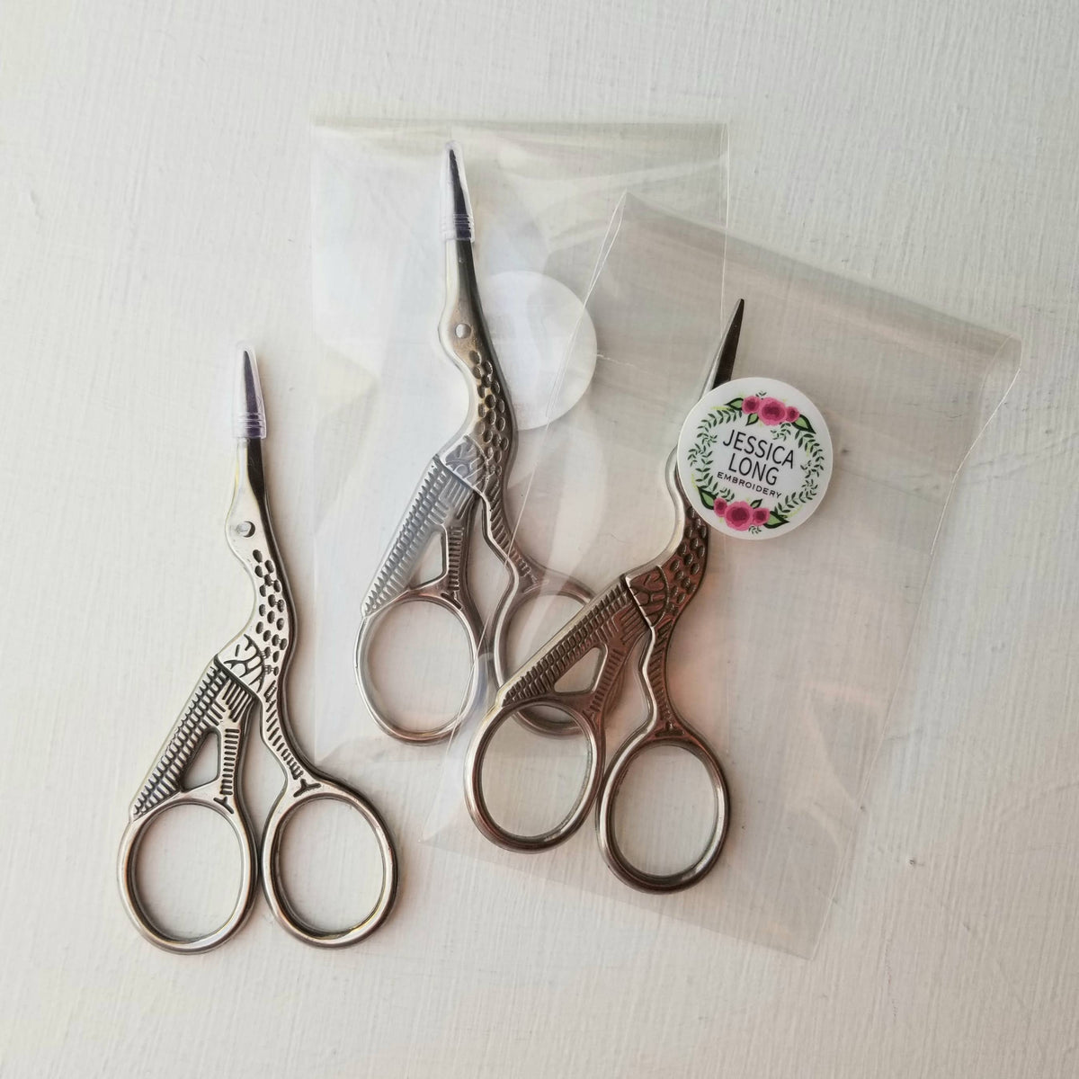 Three pairs of stork embroidery scissors, two in clear packaging