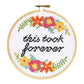 Finished cross stitch reading "this took forever" in black script with bright floral corners