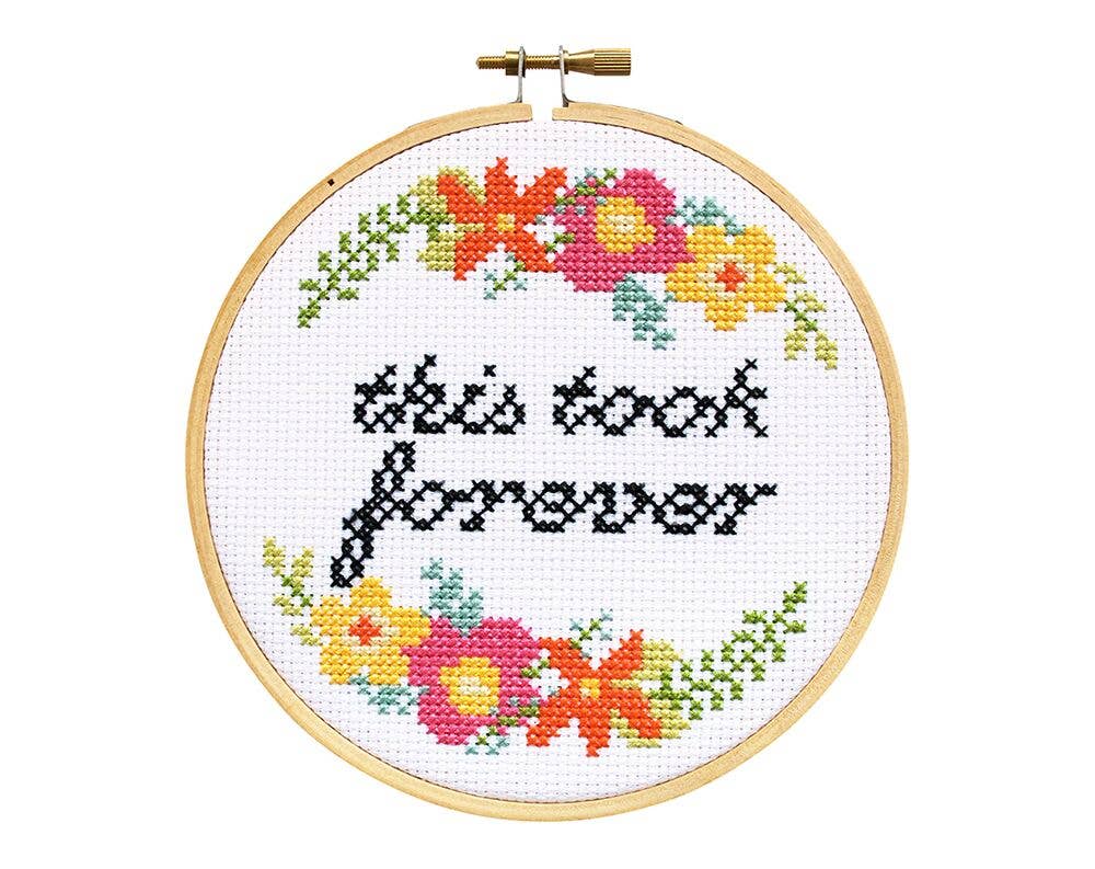 Finished cross stitch reading "this took forever" in black script with bright floral corners