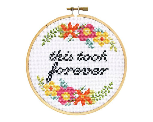 Finished cross stitch reading "this took forever" in black script with bright floral corners