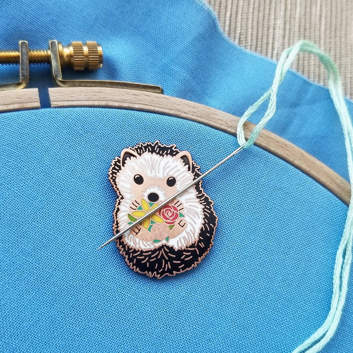 Hedgehog needle minder holding a needle with mint floss on blue fabric