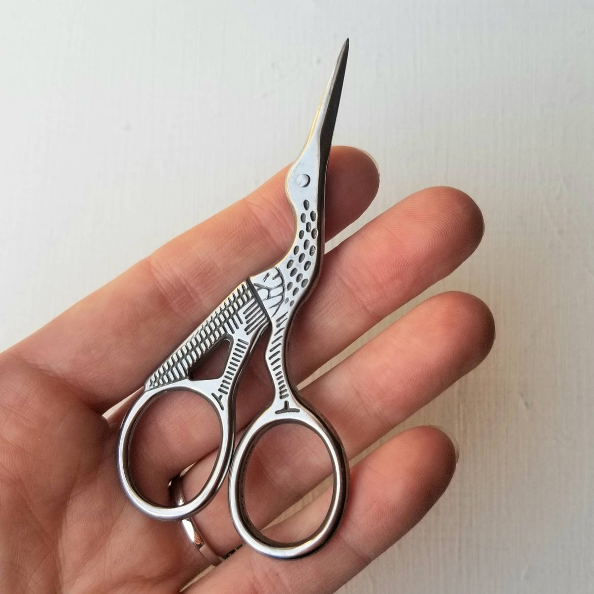 Silver stork embroidery scissors lying across an open hand