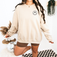 Model wearing a sand crewneck with a small smiley face on the front chest