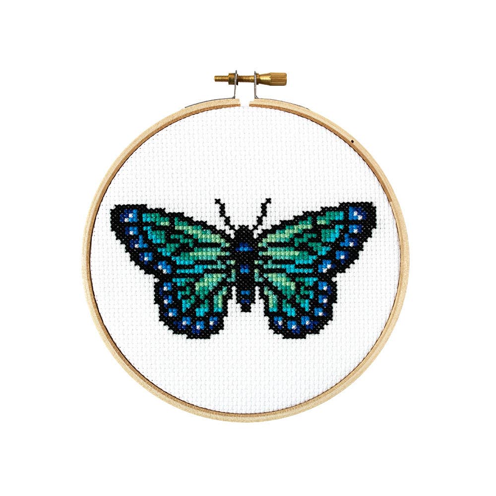 Finished butterfly cross stitch in teal, green and blue on white fabric in a wooden hoop