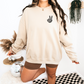 Model wearing a sand crewneck with a small peace-sign hand on the front chest