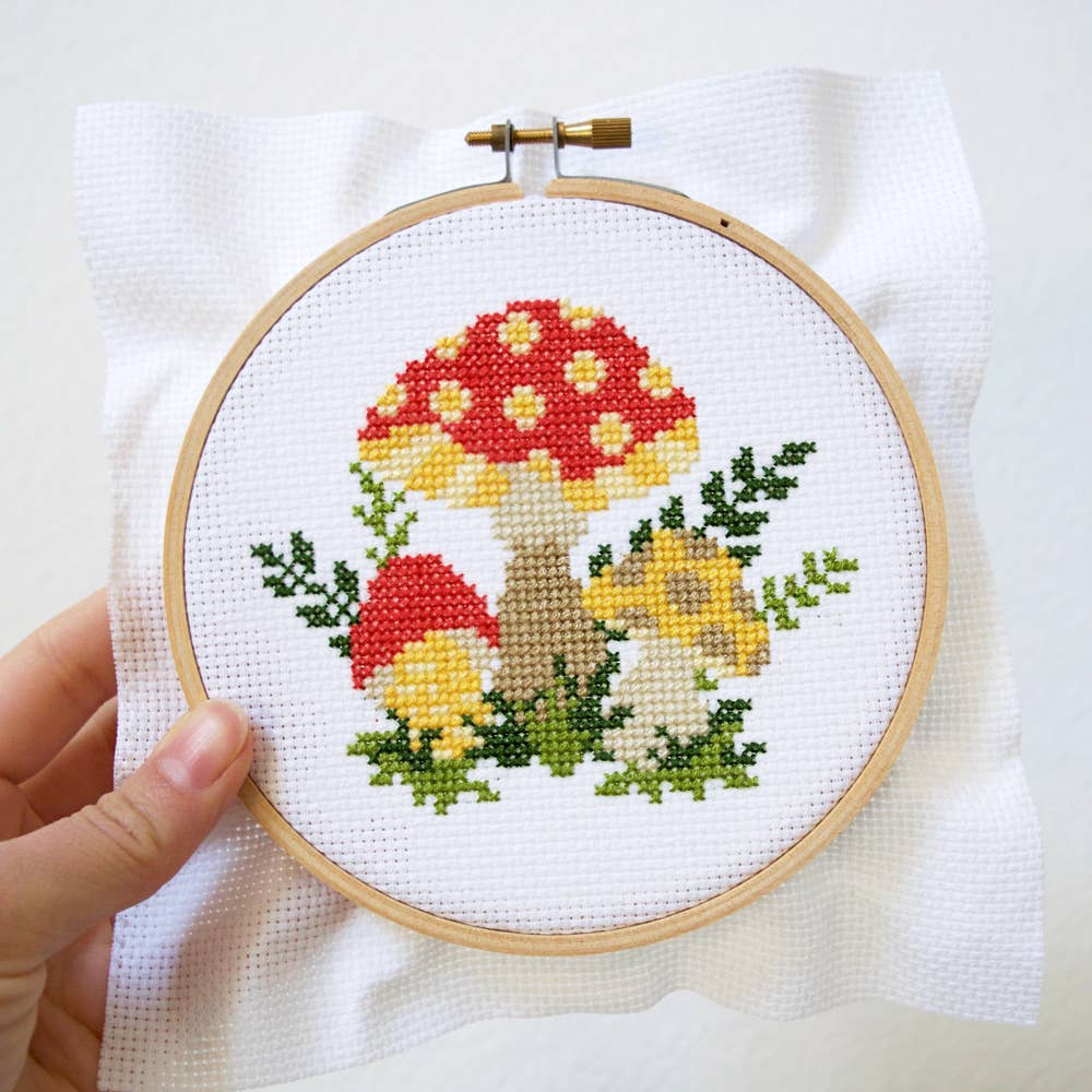 Hand holding the finished mushroom cross stitch in its hoop