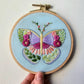 Hand holding the finished butterfly sampler in a wooden hoop