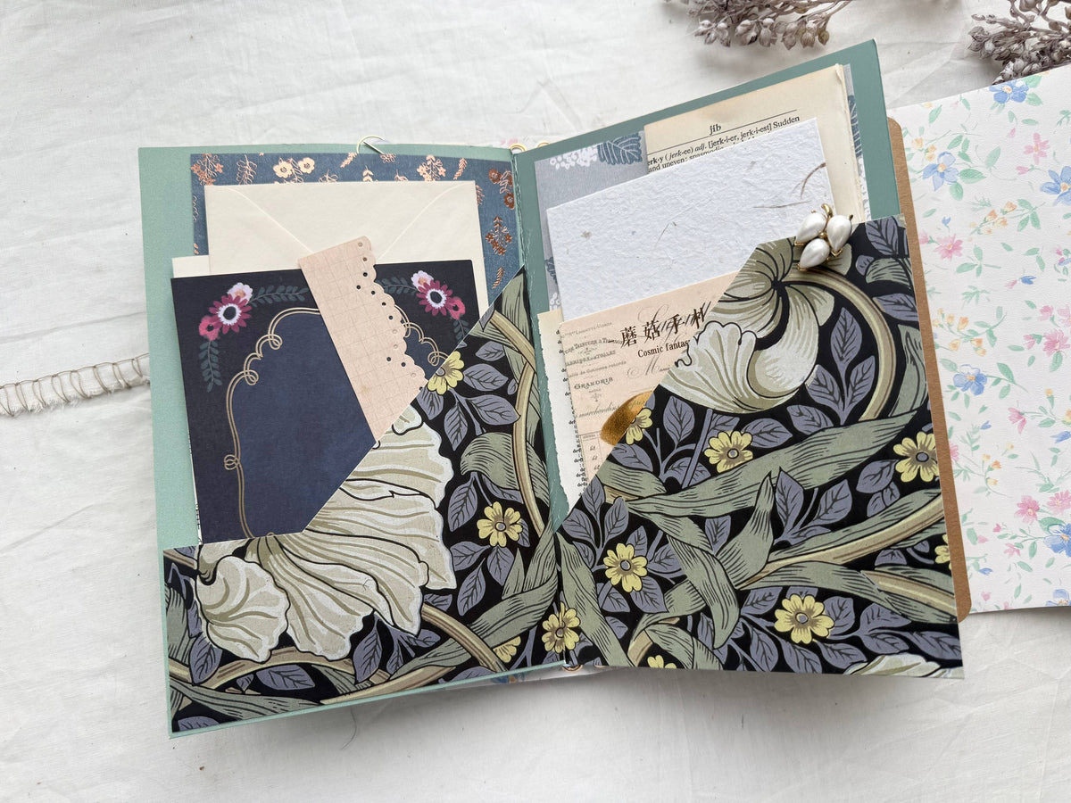Open journal folio with navy floral pockets full of vintage papers, cards and a floral tag