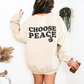 Back of a sand crewneck with "Choose Peace" in bold wavy black letters and a peace-sign hand