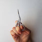 Hand holding the stork embroidery scissors upright against a white wall