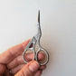 Hand holding the silver stork scissors, showing the engraved feather detail