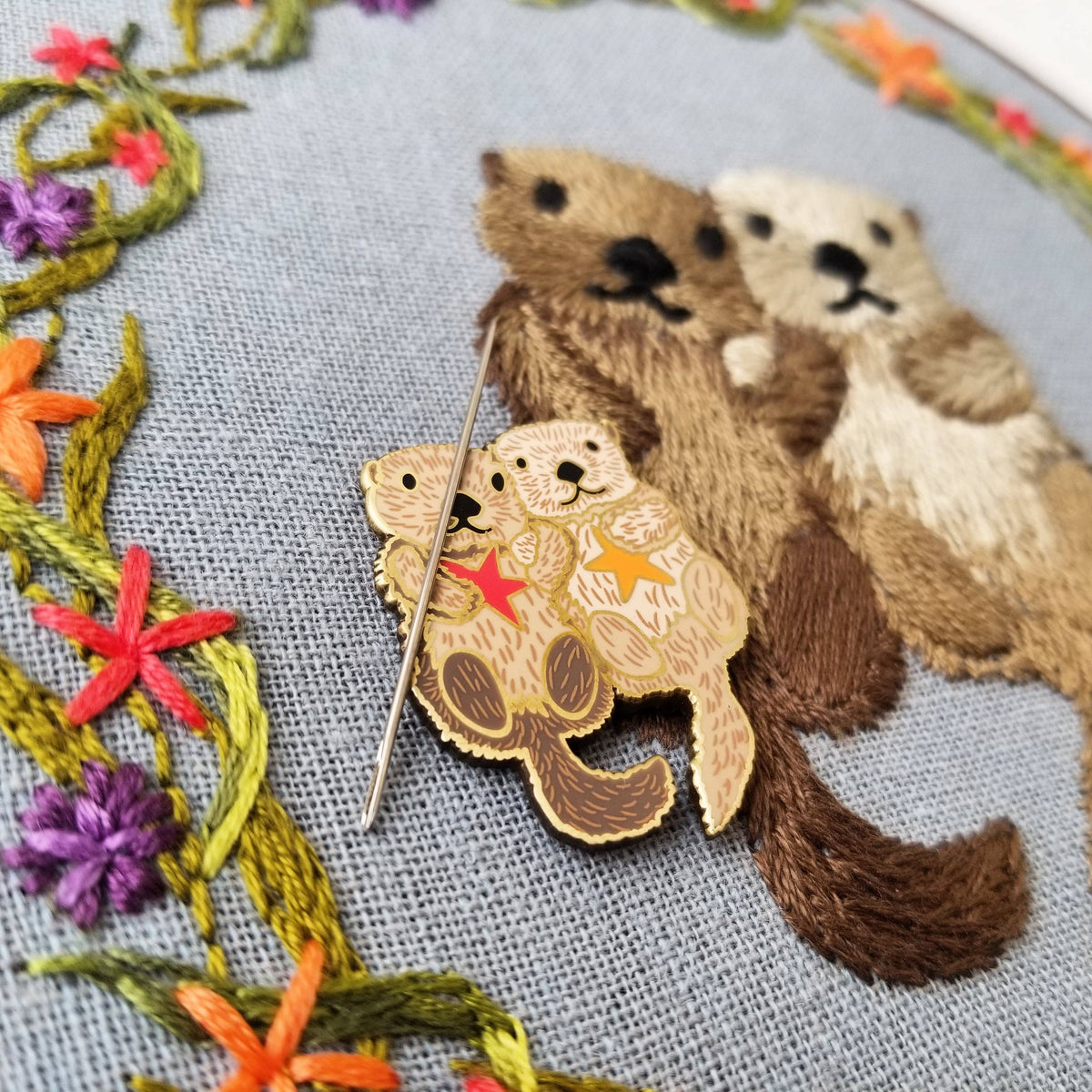 Sea otters needle minder holding a needle on the embroidered otter hoop