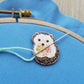 Hedgehog needle minder holding a threaded needle on blue fabric in an embroidery hoop