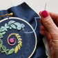 Hand stitching the spiral sampler on navy fabric in a wooden hoop