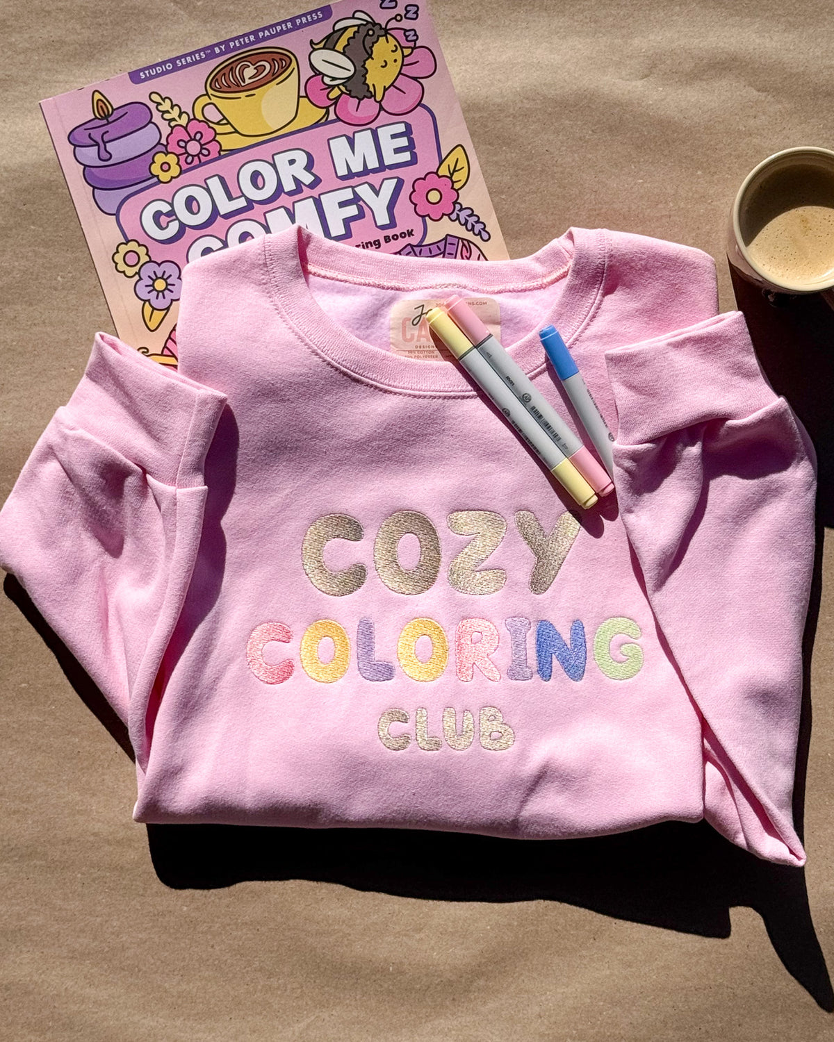 Pink Cozy Coloring Club crewneck with pastel lettering, markers and a Color Me Comfy coloring book