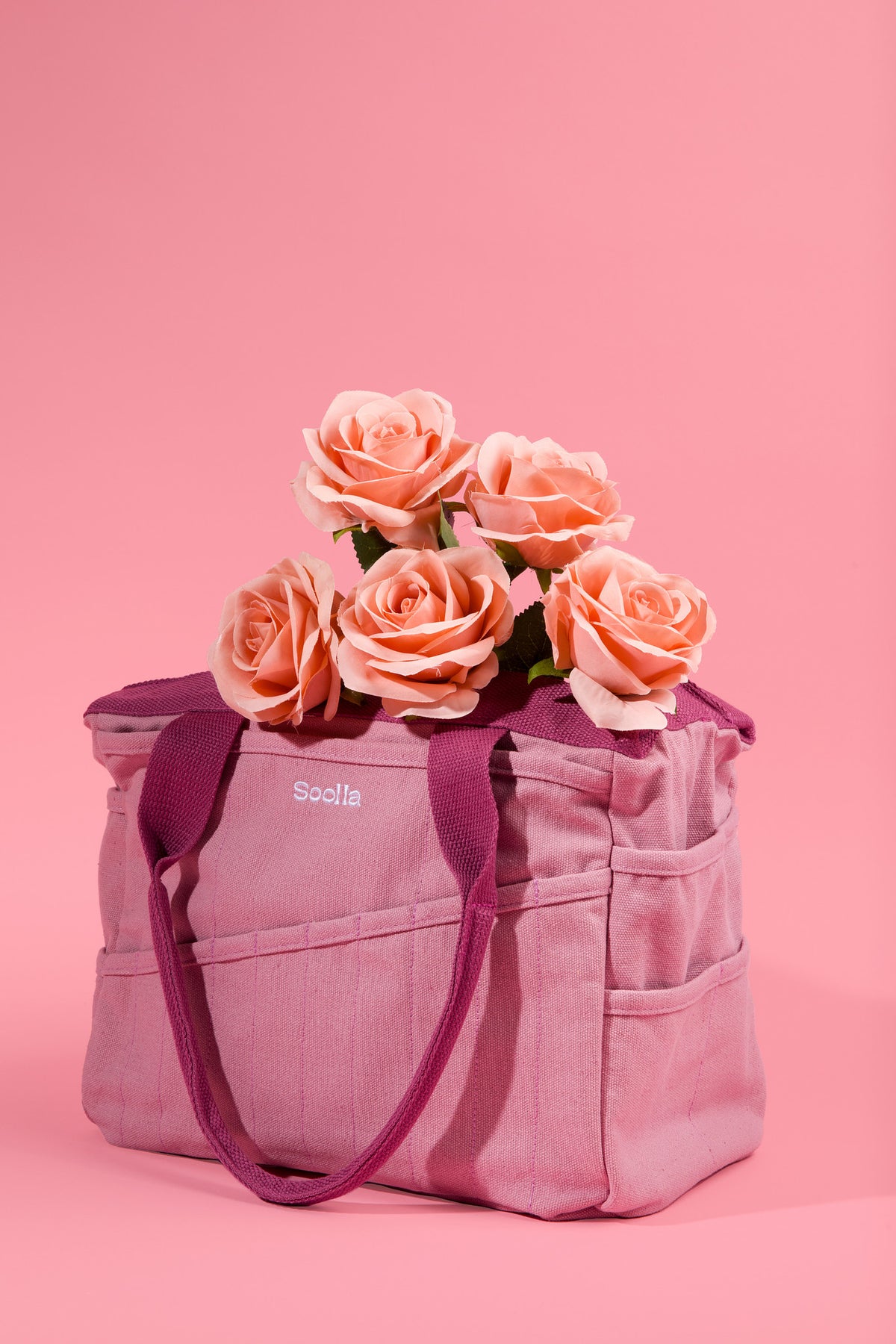 Dusty pink Soolla craft bag filled with peach roses on a pink background
