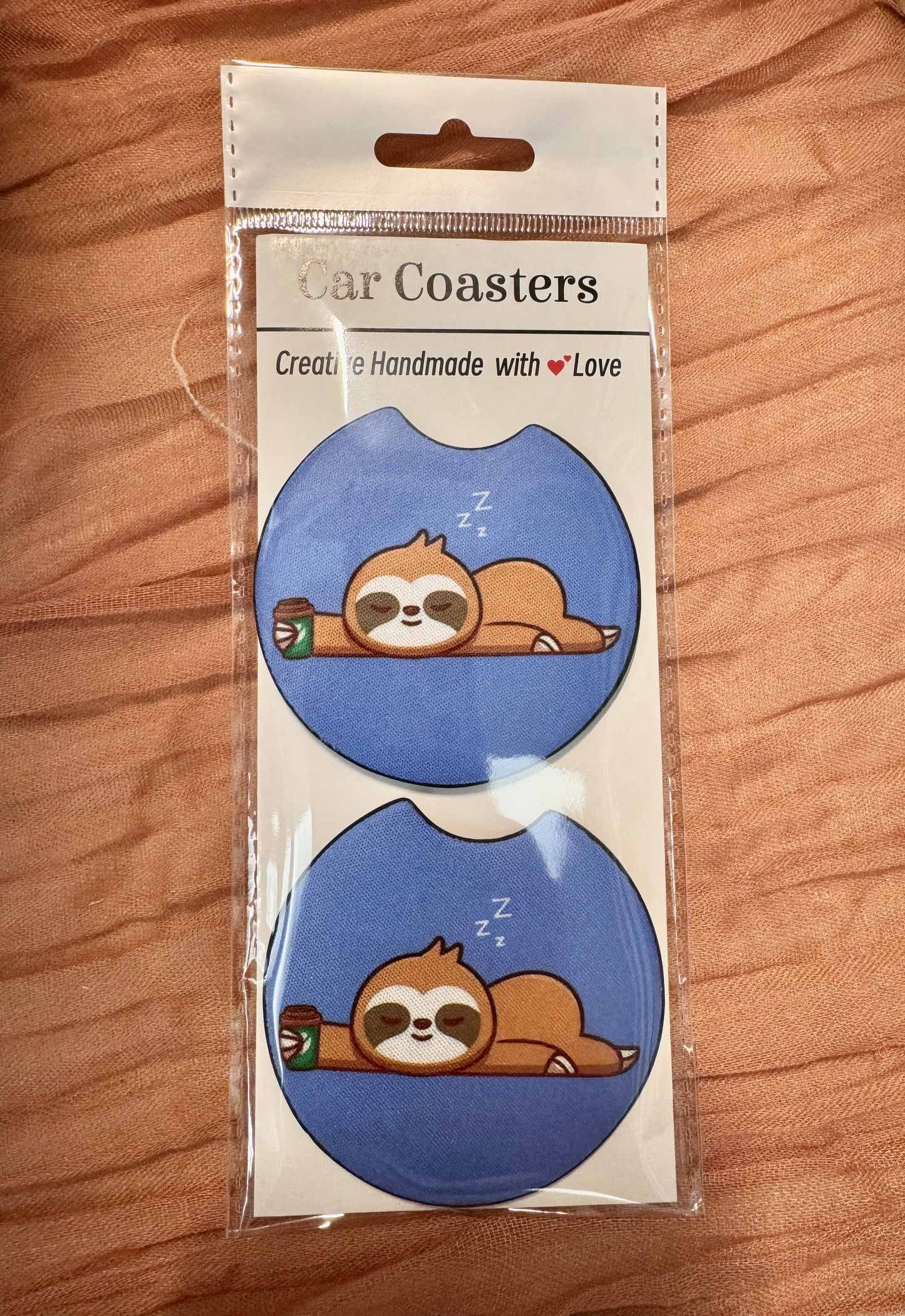 Pair of blue car coasters with a sleepy sloth next to a coffee cup