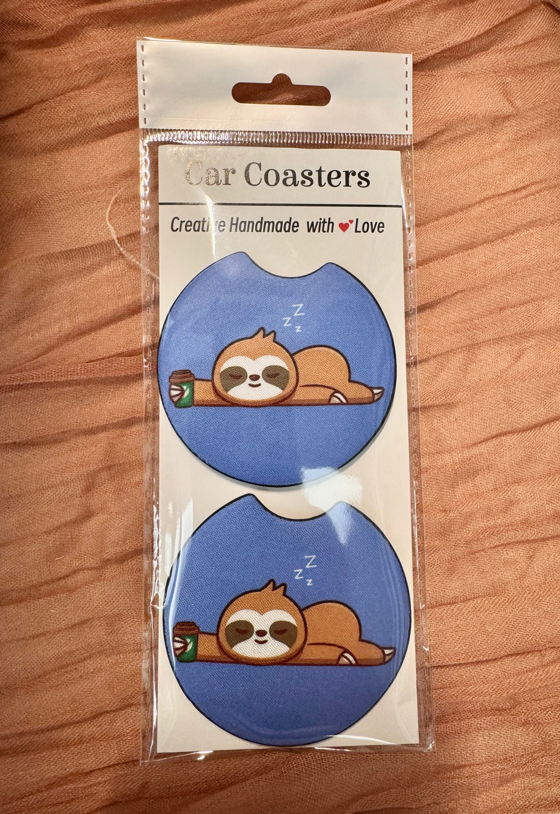 Pair of blue car coasters with a sleepy sloth next to a coffee cup