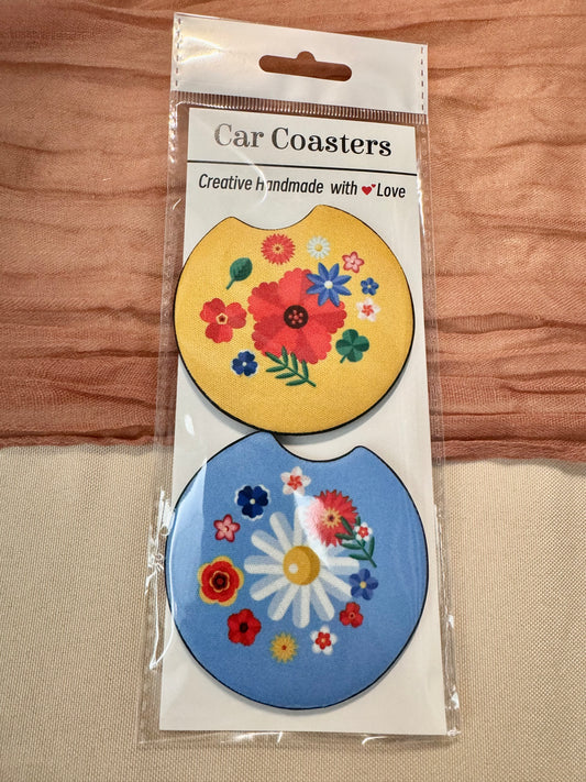 Pair of car coasters in retail packaging: yellow with a red flower bouquet and blue with a white daisy