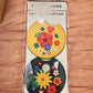 Pair of car coasters in retail packaging: yellow floral and black with a large yellow flower