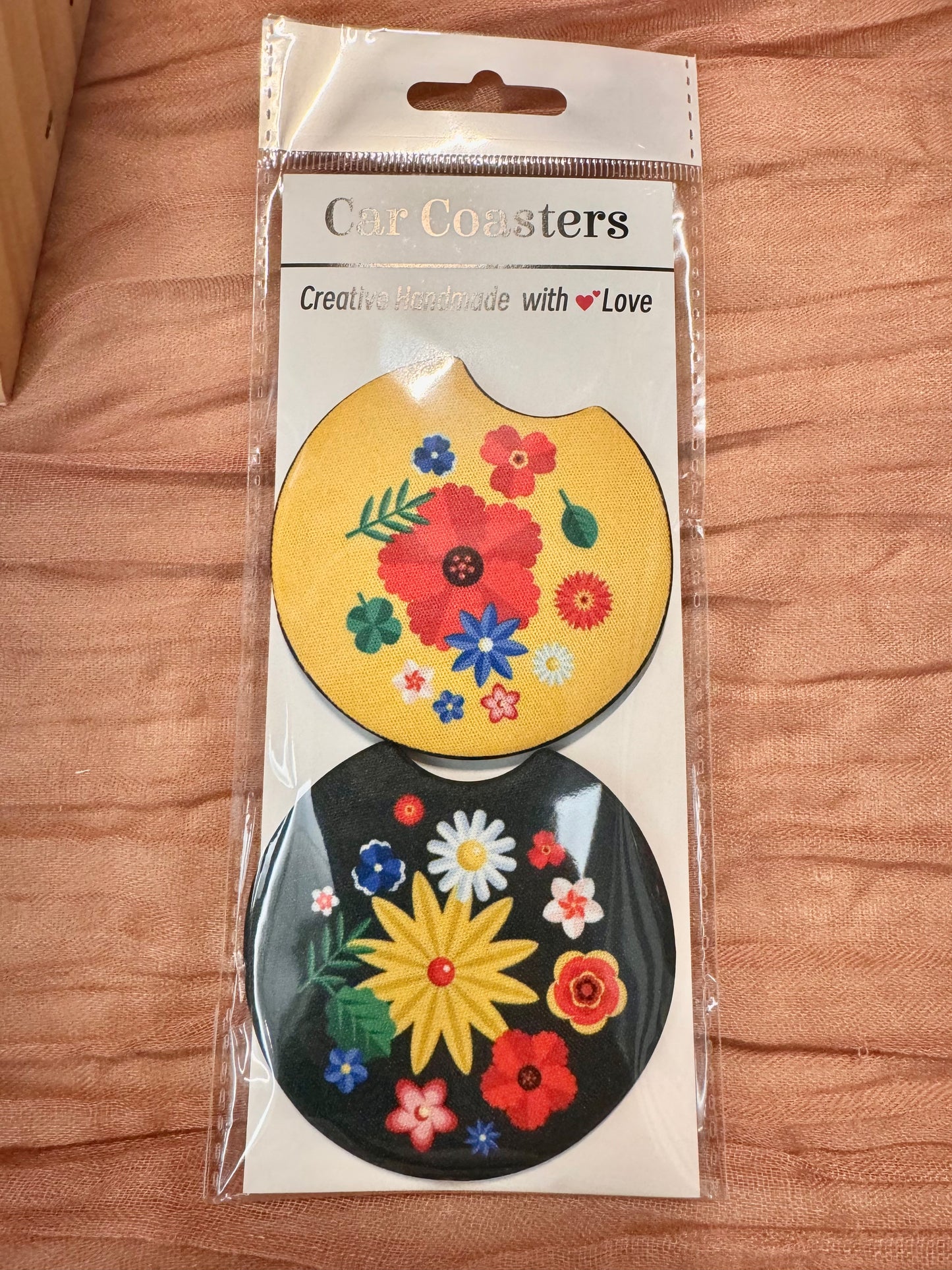 Pair of car coasters in retail packaging: yellow floral and black with a large yellow flower