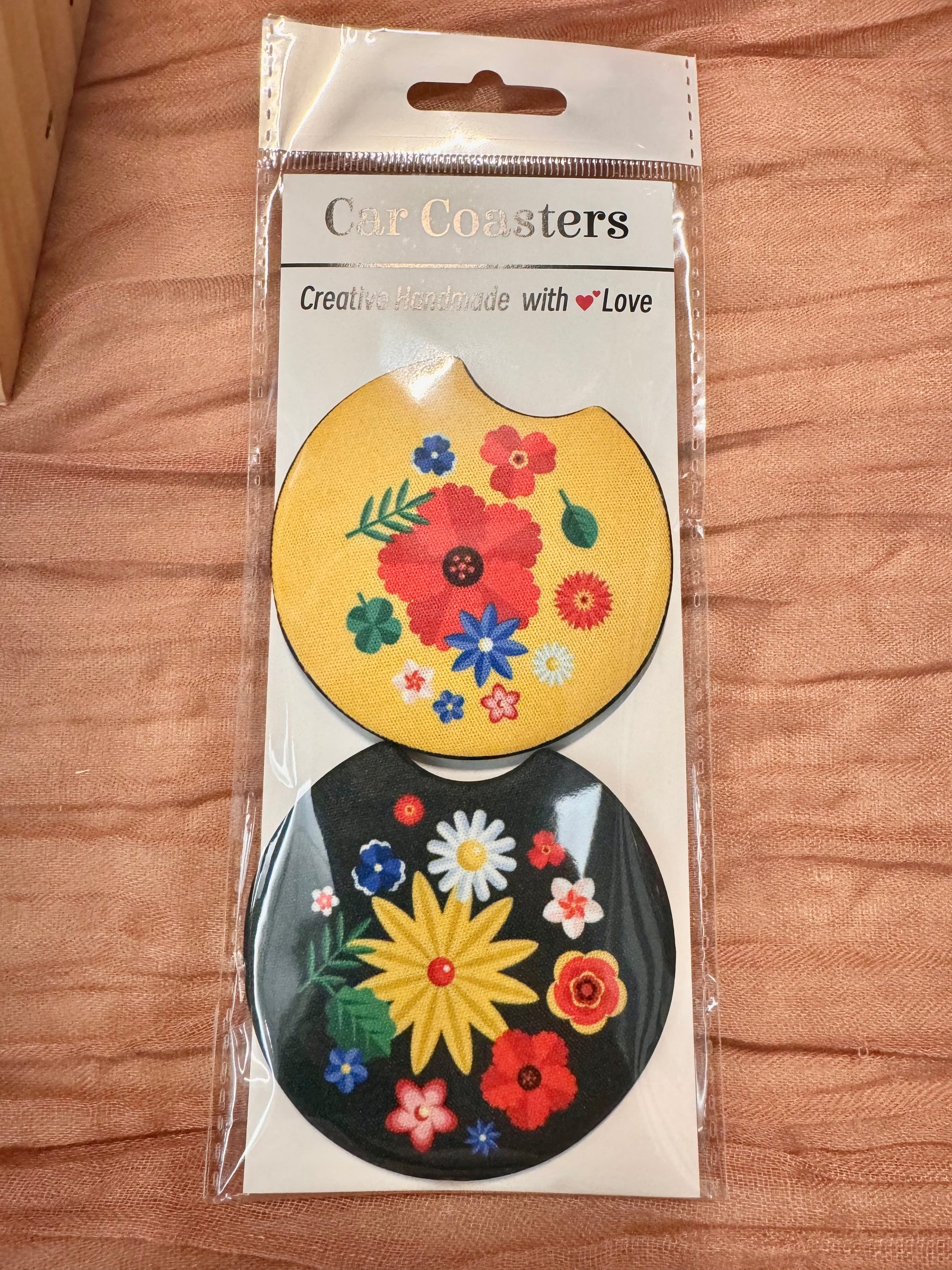 Pair of car coasters in retail packaging: yellow floral and black with a large yellow flower