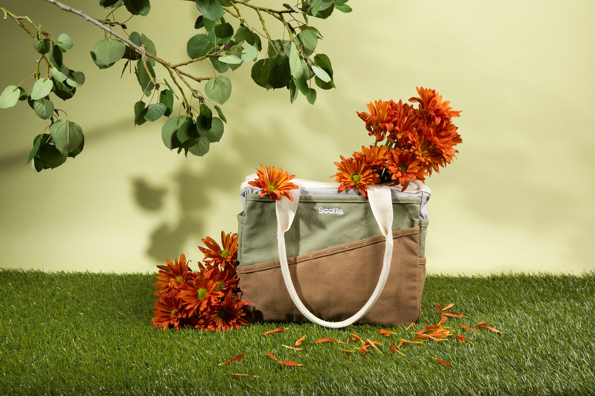 Sage and brown Soolla craft bag with orange chrysanthemums on grass under eucalyptus branches