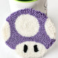 Purple and white punch needle mushroom coaster leaning against a mug