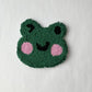 Green punch needle winking frog face coaster on a white background