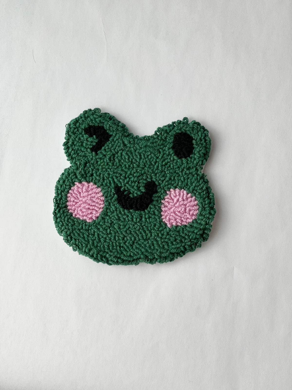 Green punch needle winking frog face coaster on a white background