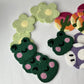Stacks of punch needle coasters: winking frogs, green daisies, cactus sunsets and a purple mushroom