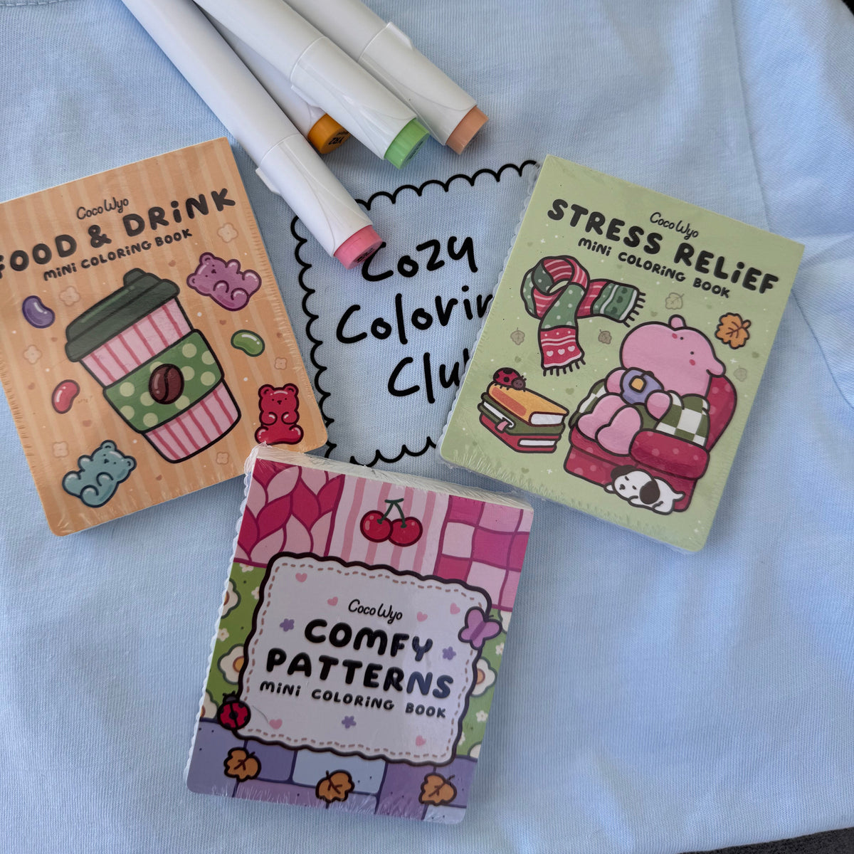Coco Wyo Food & Drink, Stress Relief and Comfy Patterns mini coloring books on a Cozy Coloring Club tee