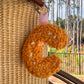 Orange punch needle letter C bag charm with white speckles, clipped to a woven straw bag