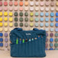 Craft bag with carving tools in the front pockets, in front of a wall of color swatches