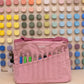 Dusty pink Soolla craft bag with carving tools in its pockets, in front of a wall of color swatches