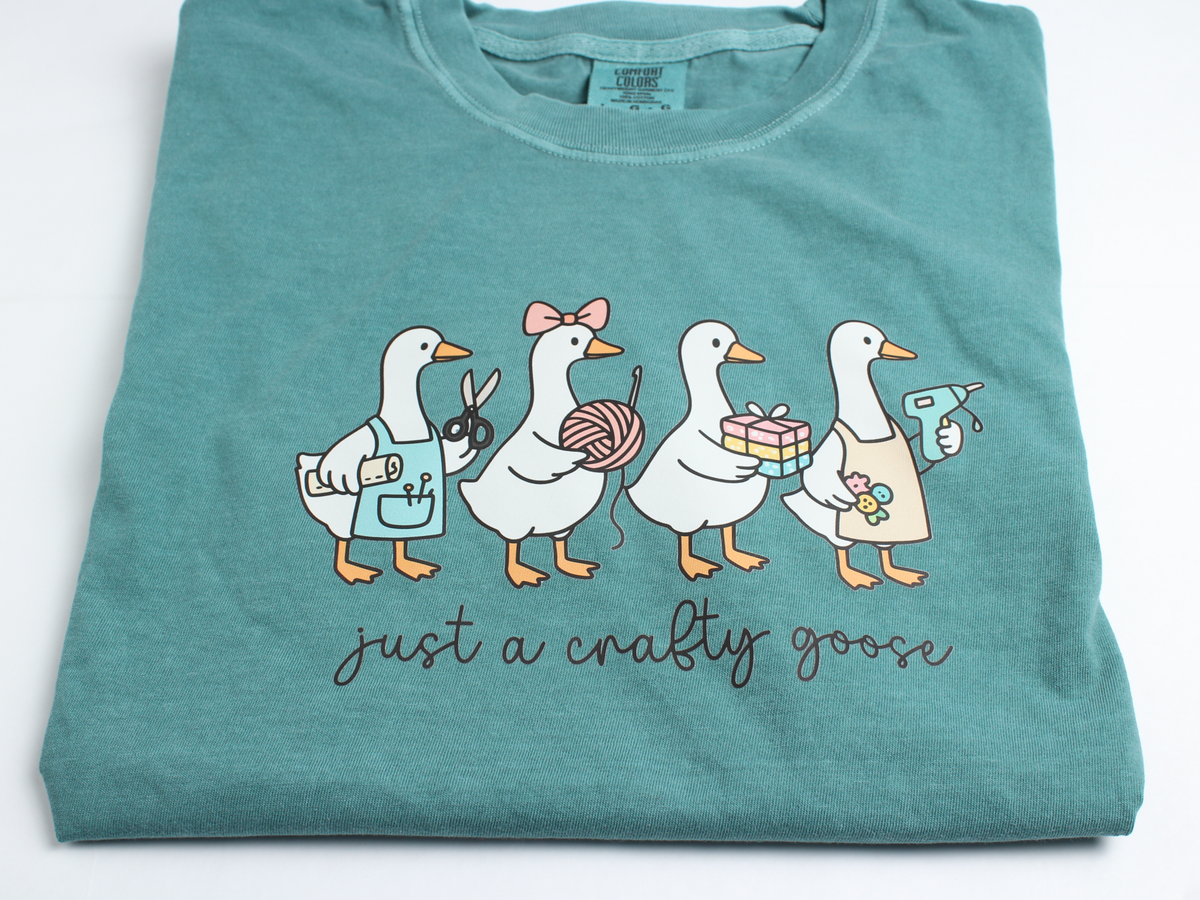 Close-up of the crafty geese print: geese holding scissors, yarn, a gift box and a glue gun