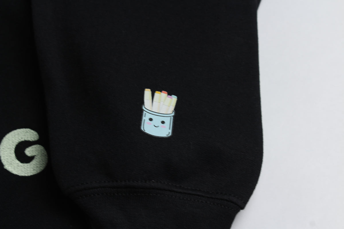 Close-up of the smiling marker-cup design on the black crewneck's sleeve