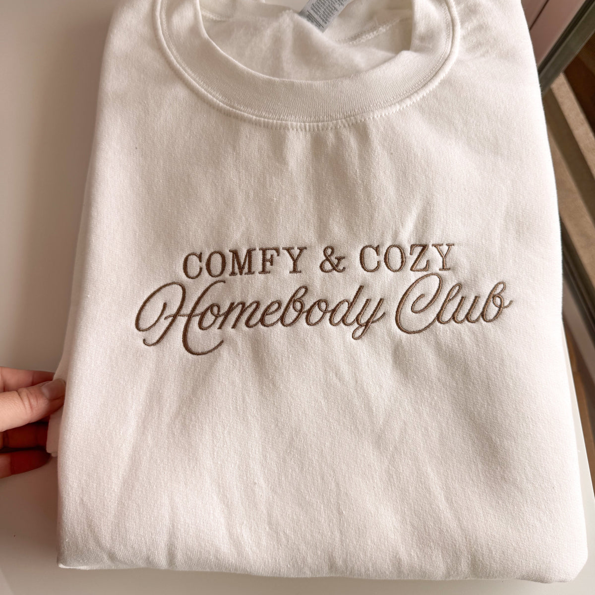 Folded white Homebody Club crewneck with brown embroidery