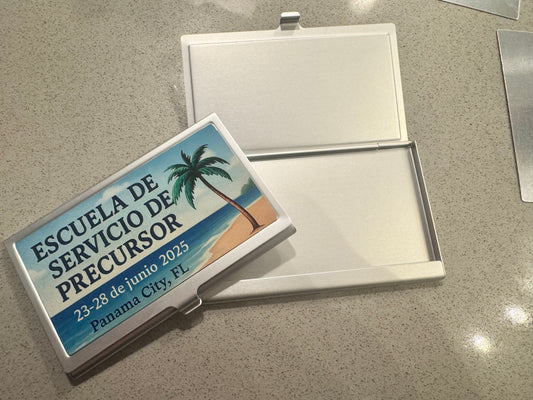 Open silver business card case with a printed lid showing a beach, palm tree and Escuela de Servicio de Precursor, Panama City, FL