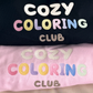 Close-up of the pastel Cozy Coloring Club embroidery on black and pink crewnecks