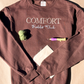 Brown Comfort Hobby Club crewneck laid flat with green yarn, a punch needle and fabric