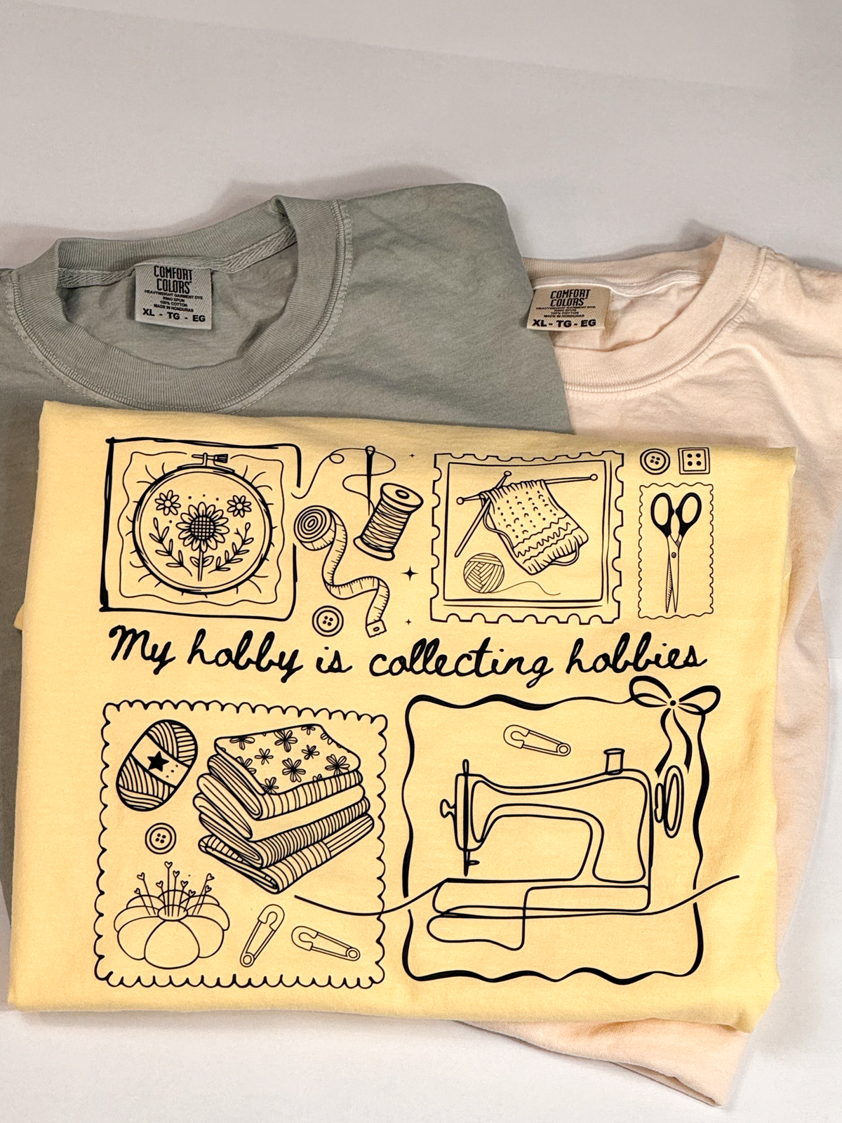 Butter yellow Hobby Collector tee printed "My hobby is collecting hobbies" with embroidery, knitting and sewing icons, on sage and peach tees
