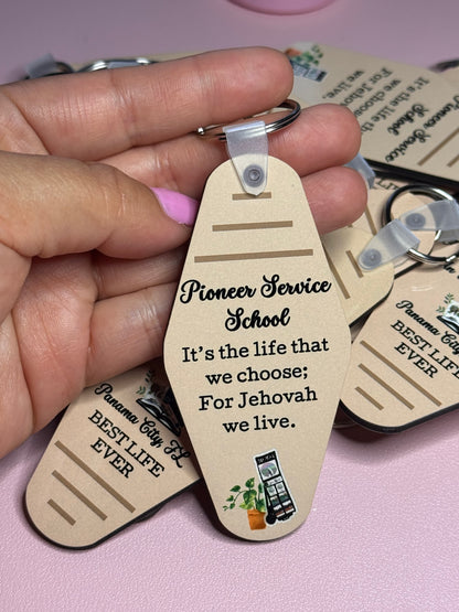Hand holding a tan motel-style keychain reading "Pioneer Service School, It's the life that we choose; For Jehovah we live"